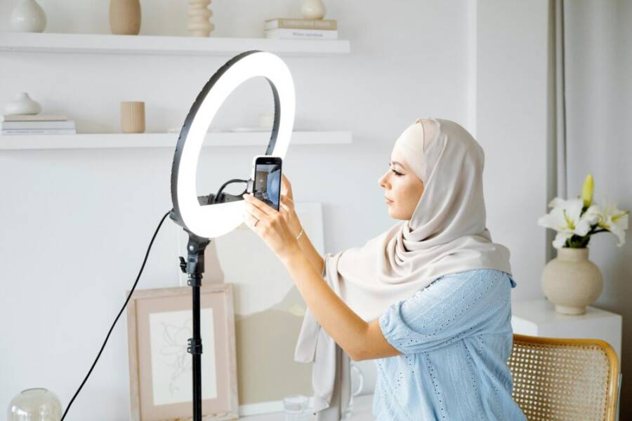 Muslim woman in hijab setting up smartphone with ring light in a modern interior