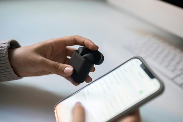 Close-up view of hands connecting wireless earbuds to a smartphone, emphasizing modern technology.