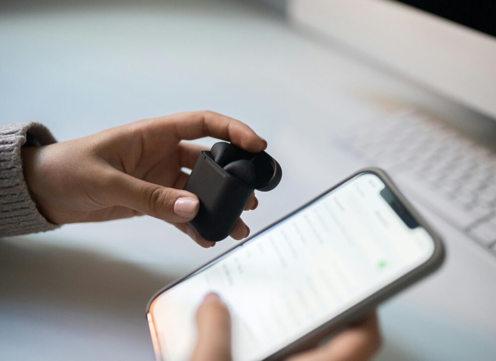 Close-up view of hands connecting wireless earbuds to a smartphone, emphasizing modern technology.