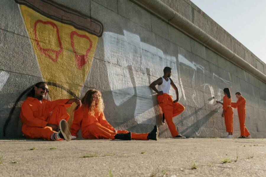 Five people in orange coveralls painting a wall outdoors, showcasing teamwork and diversity.