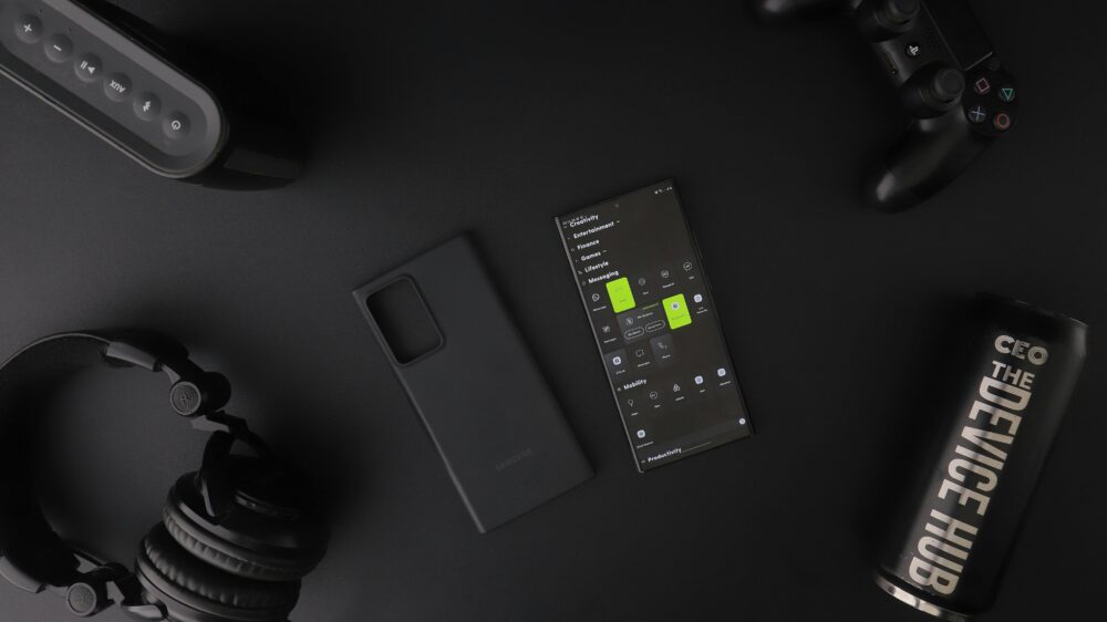 Overhead view of black modern electronics including smartphone, headphones, speaker, and controller on a table