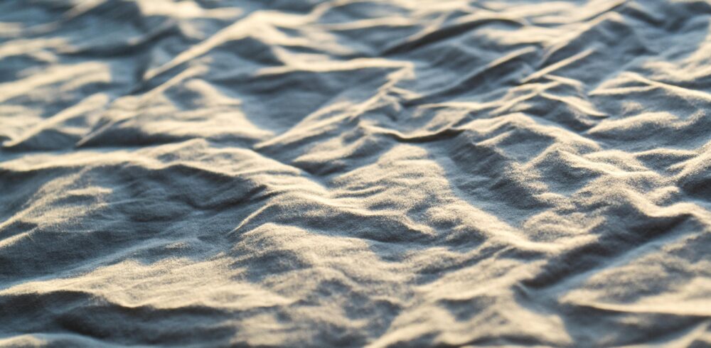 Close-up of wrinkled fabric texture illuminated by soft natural light, creating shadows and patterns