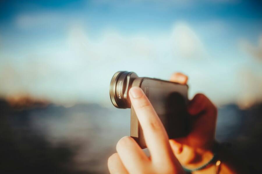 A close-up of hands using a smartphone with a lens to capture outdoor images, against a blurred background