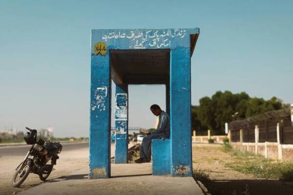晴空萬里下面，一個孤獨的人坐在鄉村公路旁的公車站。