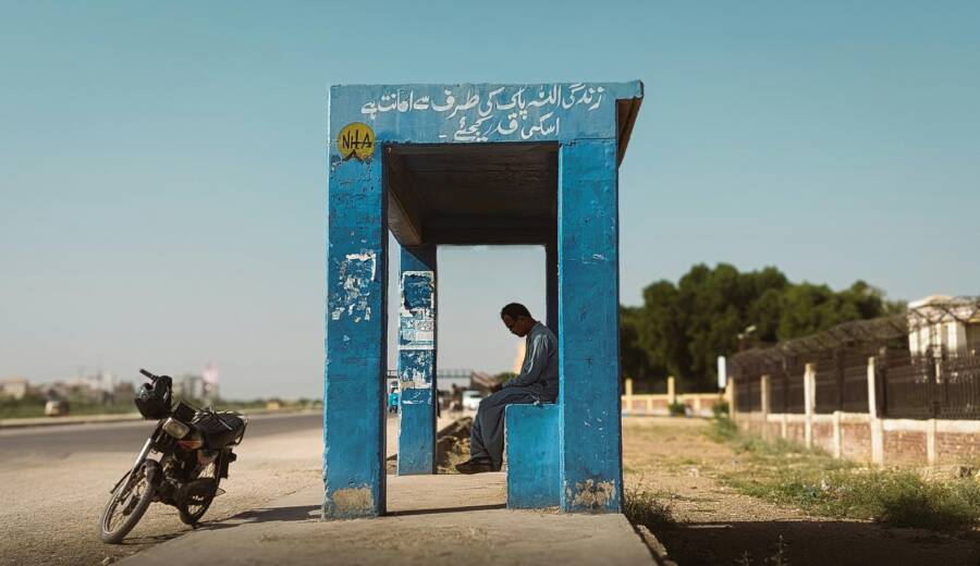 晴空萬里下面，一個孤獨的人坐在鄉村公路旁的公車站。