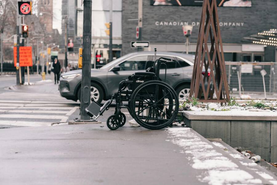 冬天，一輛輪椅停在積雪覆蓋的城市人行道上，一輛汽車從旁邊駛過。
