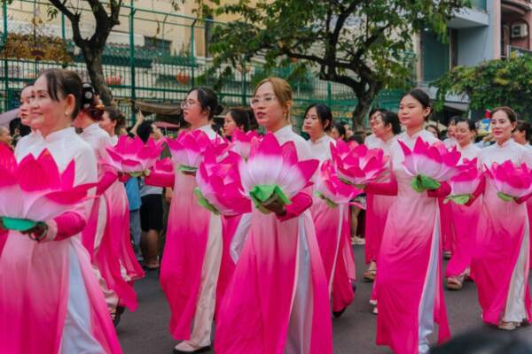 身穿粉紅色奧黛的婦女們手捧蓮花，在熱鬧的遊行隊伍中列隊行進。