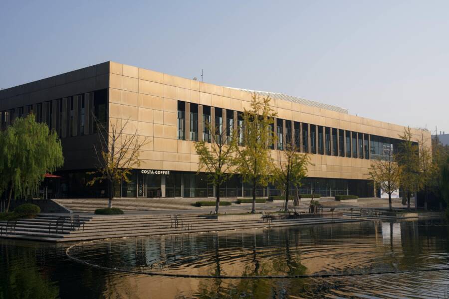 秋日的現代陽光灑在蓄水池邊，蓄水池旁綠樹成蔭，一棟建築映入眼簾。