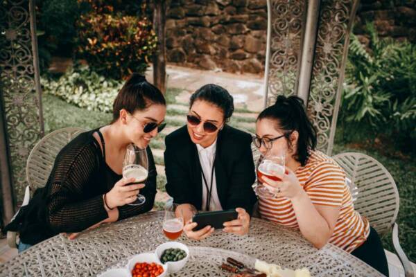 三位女士在戶外抽屜的桌子旁一邊喝一邊玩智慧型手機。