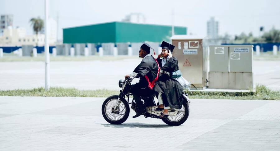 兩名身穿畢業禮服、頭戴畢業帽的畢業生騎著摩托車在戶外慶祝。