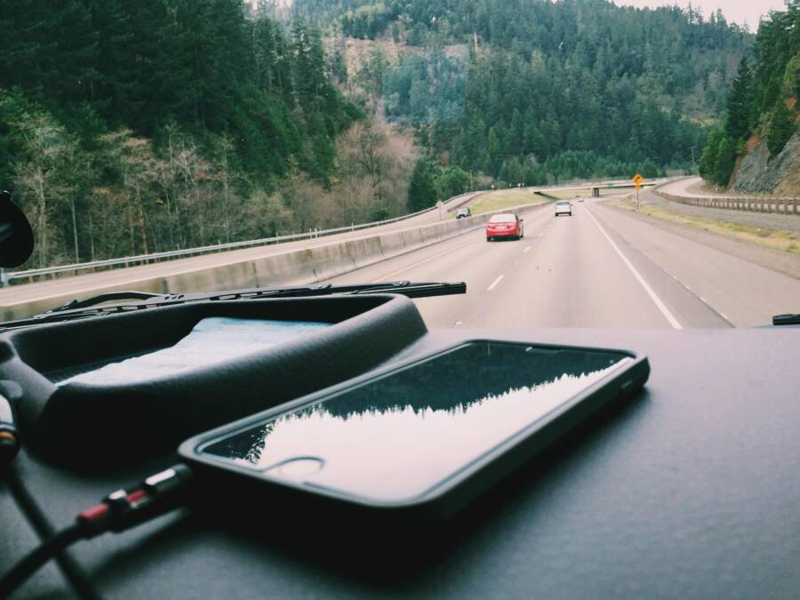 A smartphone charging on the dashboard during a scenic road trip