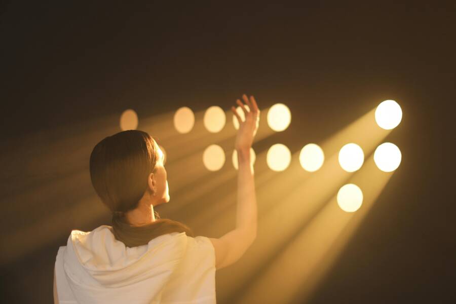 Back view of a woman reaching towards bright stage lights, capturing a dramatic moment