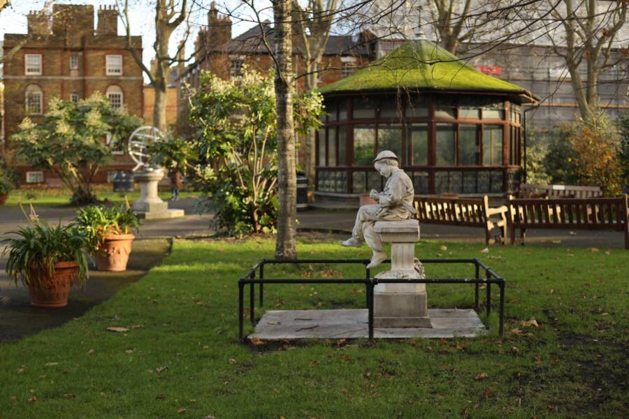 A picturesque park scene featuring a statue, pavilion, and lush greenery on a sunny day