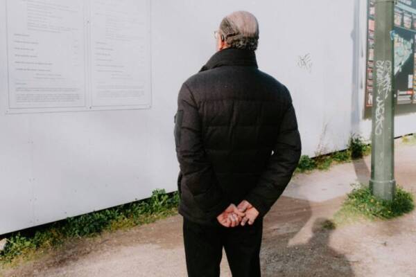 Senior man in winter jacket standing outdoors, viewing wall posters.