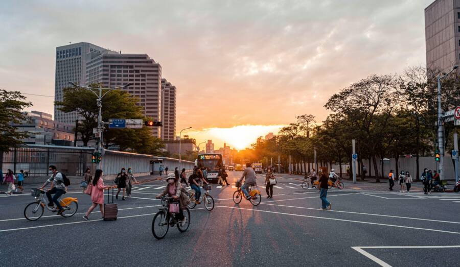 A vibrant urban scene with cyclists and pedestrians crossing a street in Taipei at sunset