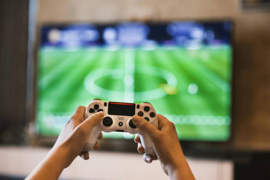 Close-up of hands holding a game controller playing a football video game on screen