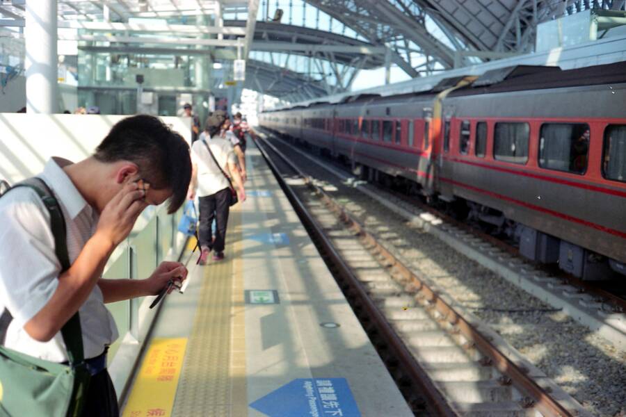 Commuters on a railway platform in Taichung, Taiwan, near a red and black train.