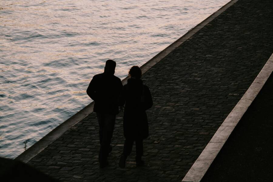 A couple walks along a riverside path at dusk, capturing a peaceful and romantic moment