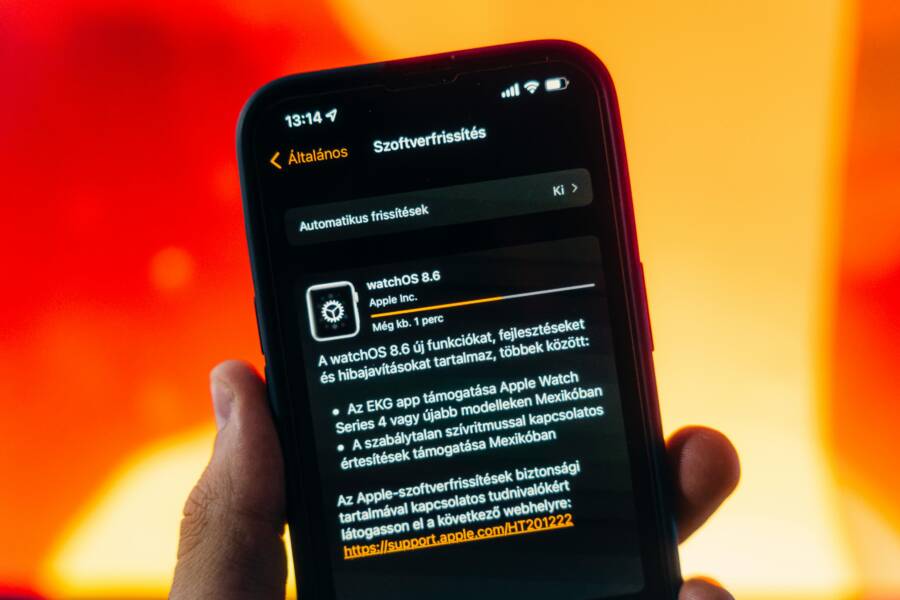 Hand holding a smartphone displaying WatchOS 8.6 update notification against warm gradient background.