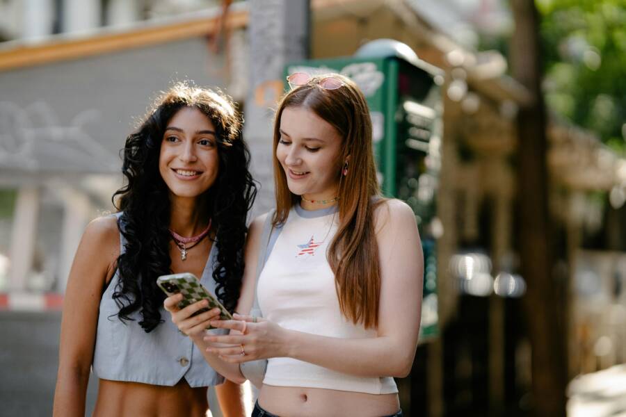 Two people outside on a sunny day with phones in hand, bright screen visible