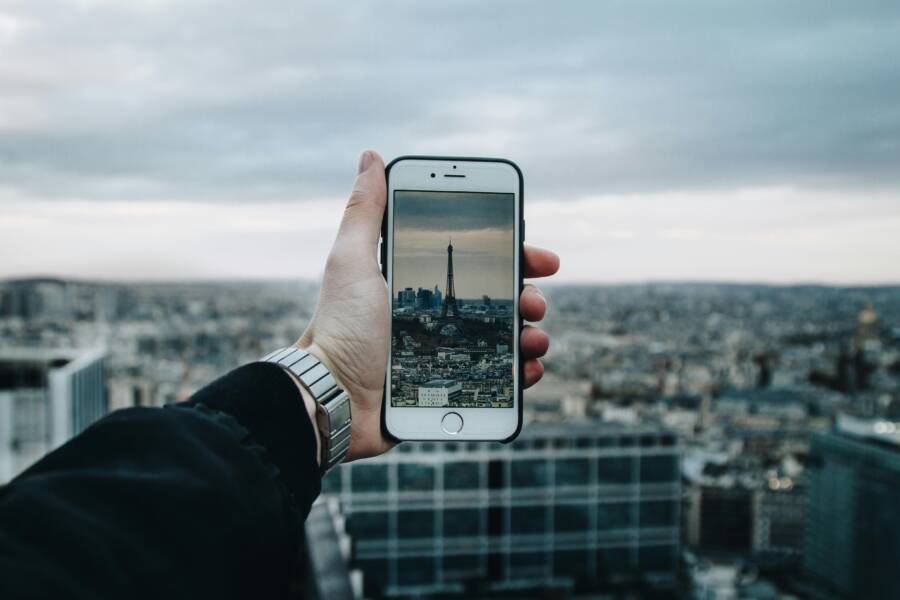 A person uses a smartphone to capture the Eiffel Tower amidst a panoramic cityscape.