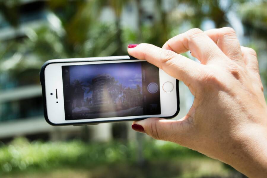 A hand holding a smartphone capturing a blurred outdoor background, highlighting phone photography