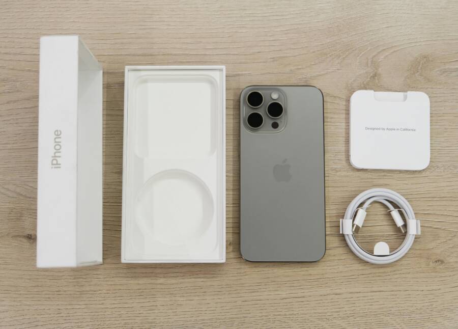 Flat lay view of the newest Apple iPhone model, box, and charging accessories on a wooden table