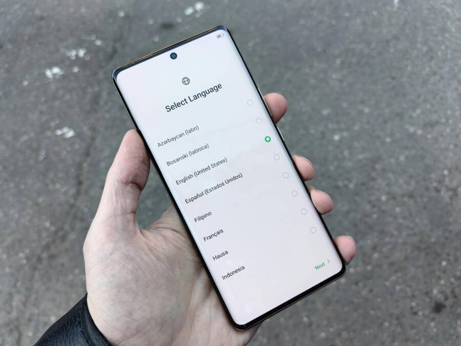 A close-up of a hand holding a smartphone showing a language selection screen outdoors in Moscow