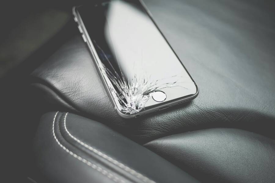 Close-up of a broken smartphone with a cracked screen on a leather car seat
