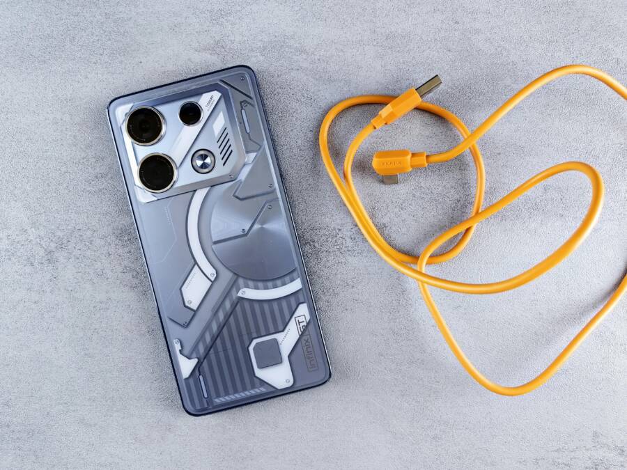 A sleek smartphone beside a bright orange charging cable on a textured surface.