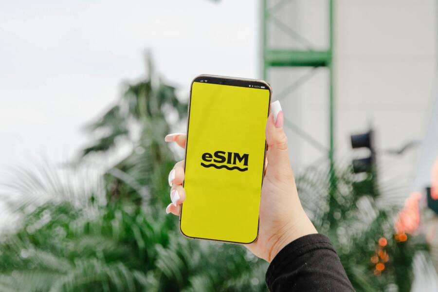 A hand holding a mobile phone displaying eSIM over a yellow screen outdoors