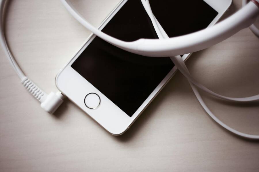 Close-up of a smartphone tangled with white earbuds on a light wooden table
