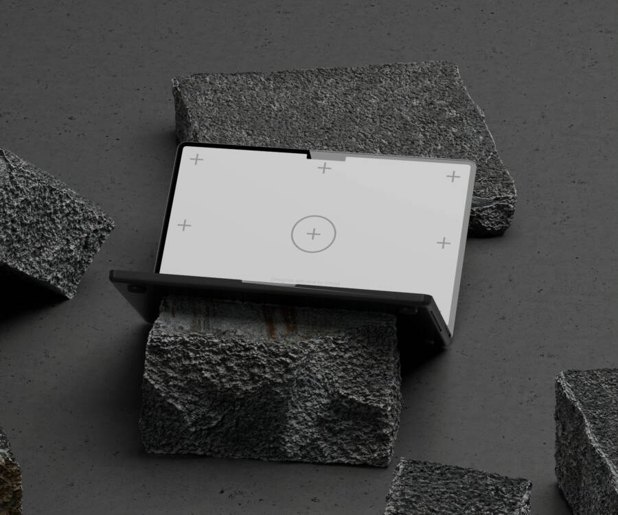 A sleek laptop with calibration screen, placed on rough stones against a gray background.