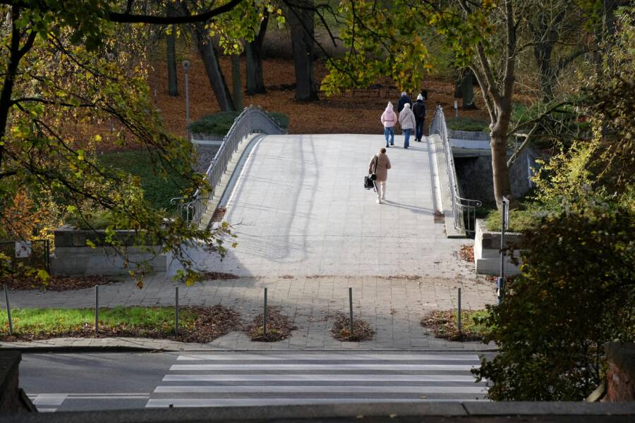 A scenic view of a bridge in a park with people walking on a sunny autumn day