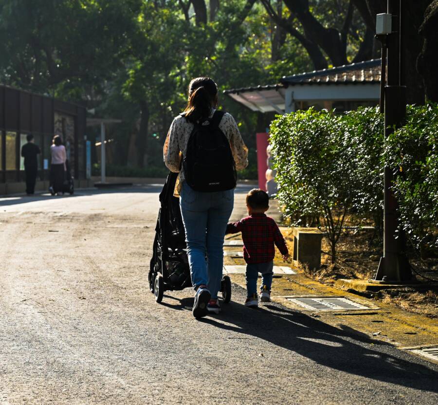 A mother and child stroll down a sunlit path, surrounded by greenery in Kaohsiung City, Taiwan.