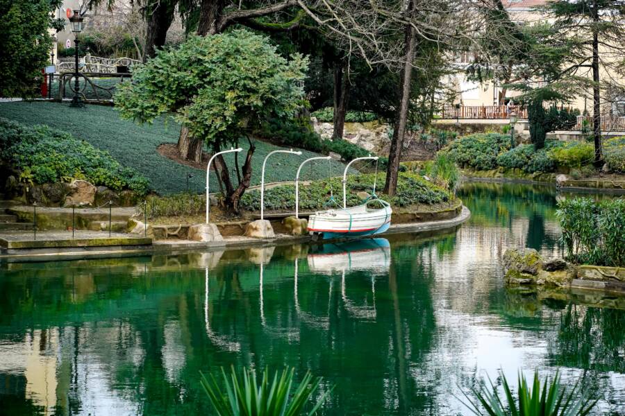 A peaceful green lake with a small boat docked near lush greenery in a tranquil park setting
