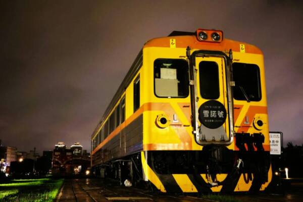 A vibrant yellow and orange train captured under city lights in Kaohsiung, Taiwan