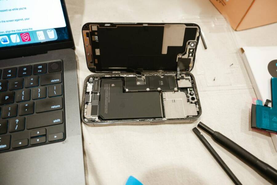 Open iPhone with repair tools and laptop, showcasing DIY battery replacement process