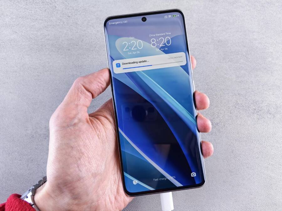 Close-up of a hand holding a smartphone with a downloading update notification on the screen.