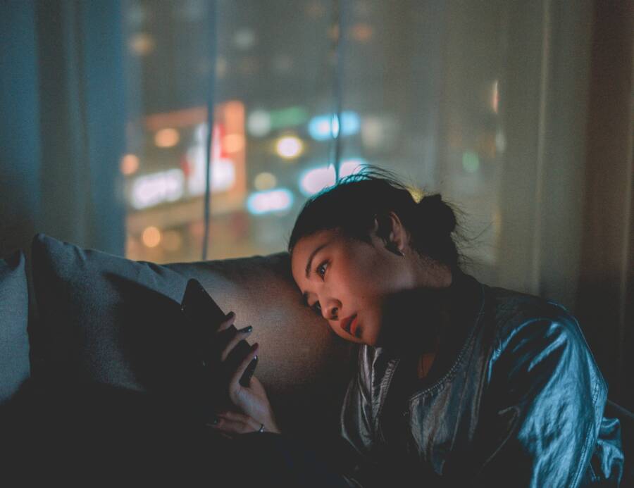 A woman looking at her mobile phone at night with city lights blurred in the background