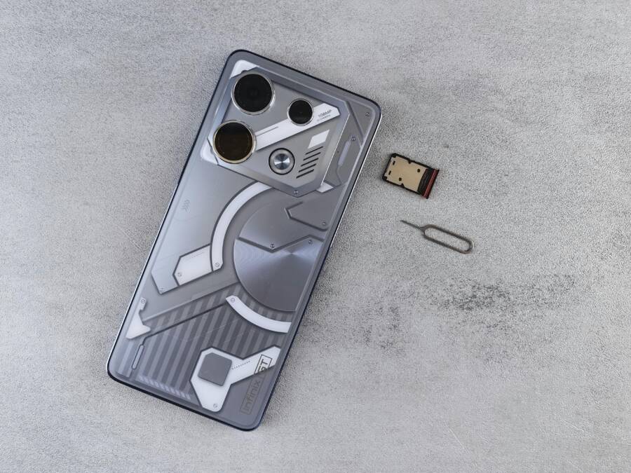 Close-up of a smartphone with futuristic design alongside a SIM card and ejector tool on a gray surface