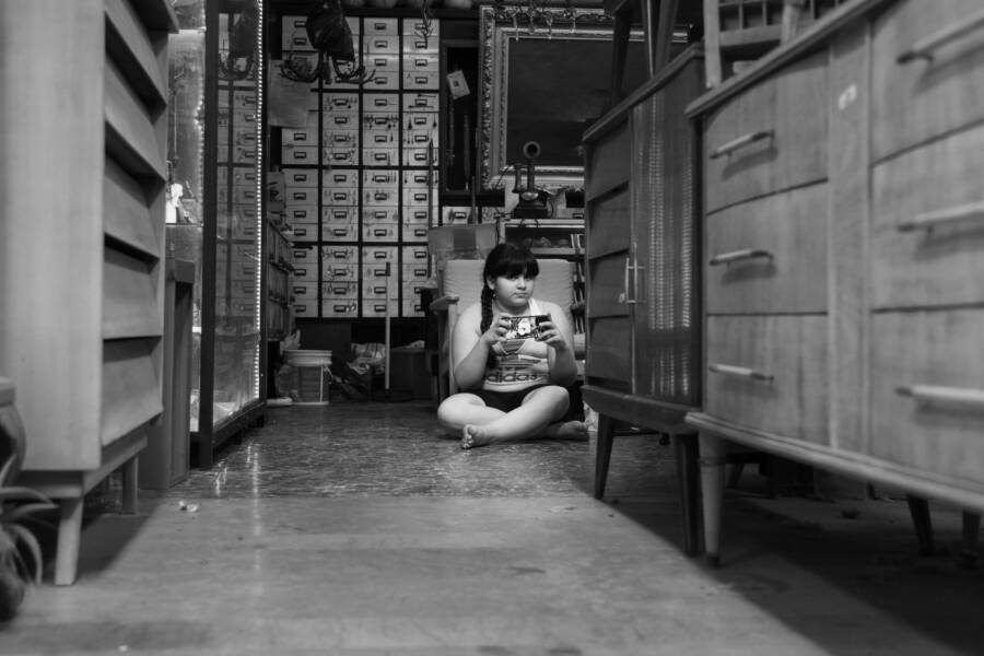 A child sits playing with a smartphone in a cluttered vintage shop filled with classic furniture