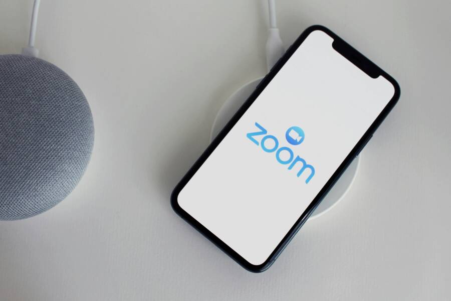 Close-up of a smartphone with Zoom app on a wireless charger next to a smart speaker