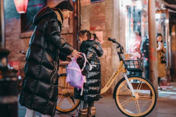 A mother helping her daughter with a backpack on a vibrant Beijing street at night