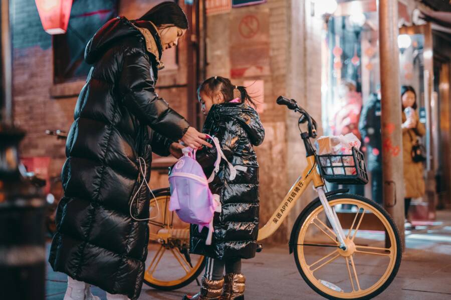 A mother helping her daughter with a backpack on a vibrant Beijing street at night