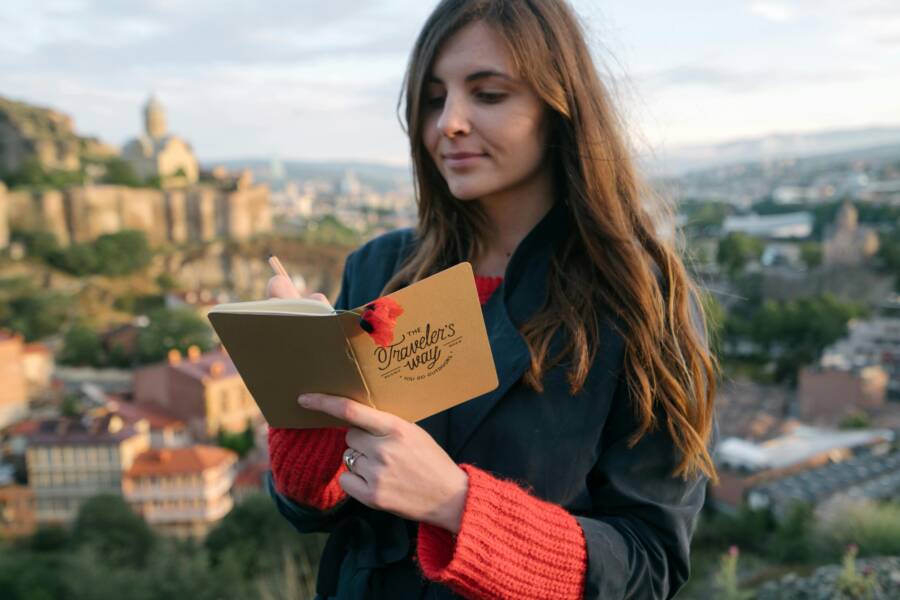 A woman writes in her journal against a backdrop of a historic cityscape