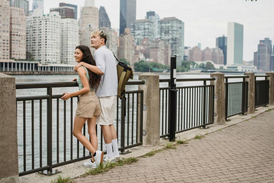 Cheerful couple resting and spending time together on promenade against skyscrapers in daytime