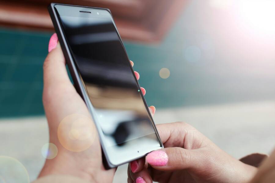 Close-up of hands holding a smartphone outdoors with a bright lens flare and reflections