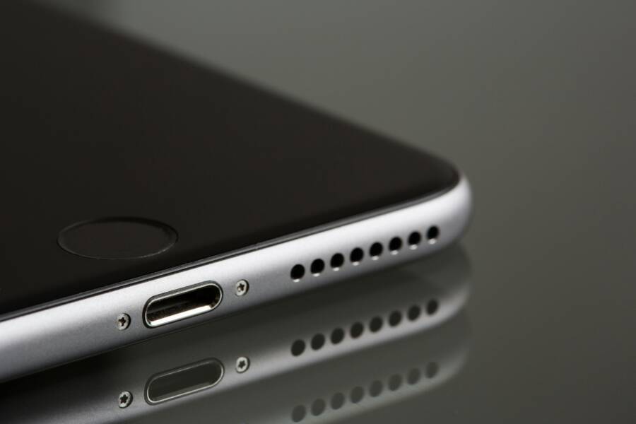 A sleek smartphone close-up highlighting its lightning connector and speaker, reflecting on a surface