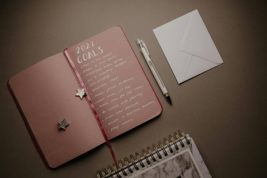 A flat lay image of an open journal with 2021 goals, pen, and envelope on a brown background